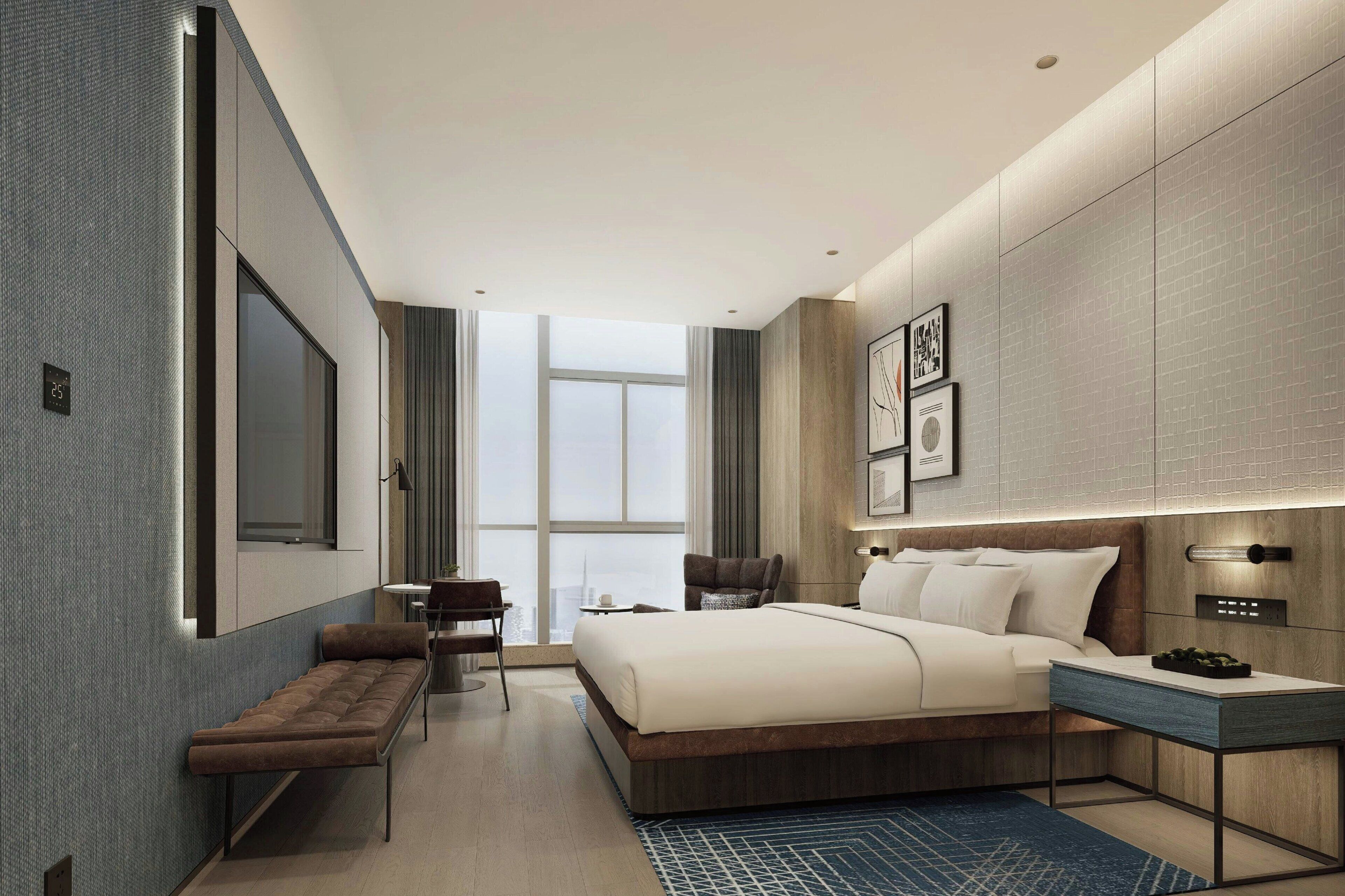 A modern hotel room with a large bed, a desk, a bench, and a view of the city.