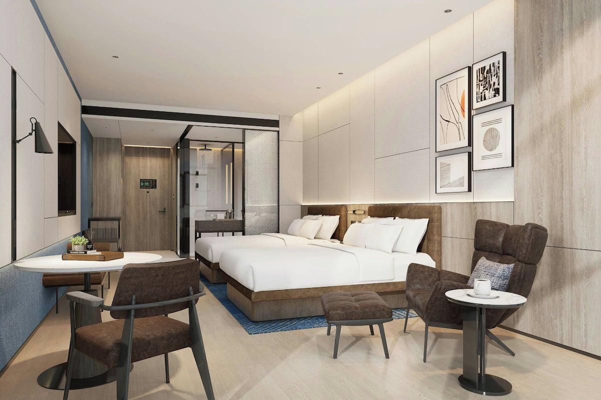 A modern hotel room with a bed, two chairs, a small table, and a sofa.