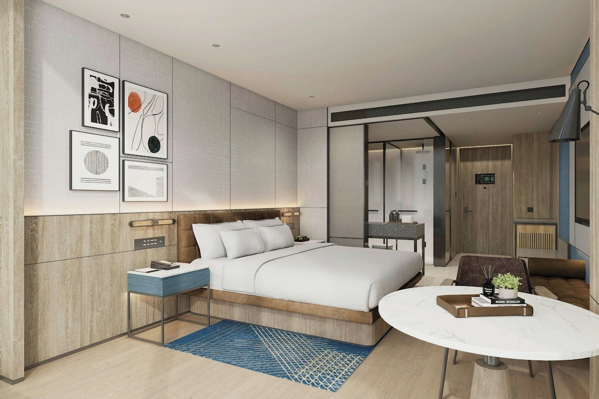 A modern hotel room with a large bed, a desk with a chair, a round dining table, and artwork on the walls.