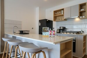 A modern kitchen with a central island, bar stools, a black refrigerator, and a stove. - w* | Modern & Cozy 2BR w/ Balcony in Miraflores (Miraflores)
