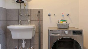 A bathroom with a white sink, a wall-mounted heater, a washing machine, and a broom. - w* | Modern & Cozy 2BR w/ Balcony in Miraflores (Miraflores)