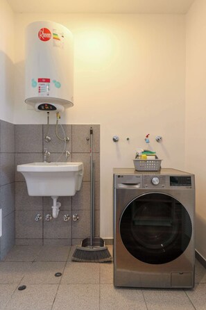 A bathroom with a white sink, a wall-mounted heater, a washing machine, and a broom. - w* | Modern & Cozy 2BR w/ Balcony in Miraflores (Miraflores)