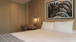 A hotel room with a bed, a desk, a chair, a lamp, and a large framed picture on the wall. - w* | Modern & Cozy 2BR w/ Balcony in Miraflores (Miraflores)
