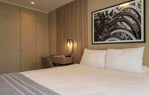 A hotel room with a bed, a desk, a chair, a lamp, and a large framed picture on the wall. - w* | Modern & Cozy 2BR w/ Balcony in Miraflores (Miraflores)