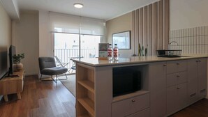 A modern kitchen with a large island, a dining area with a chair, and a TV on a wooden stand. - w* | Modern & Cozy 2BR w/ Balcony in Miraflores (Miraflores)