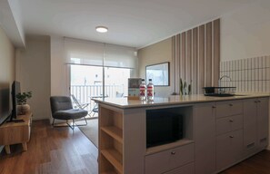 A modern kitchen with a large island, a dining area with a chair, and a TV on a wooden stand. - w* | Modern & Cozy 2BR w/ Balcony in Miraflores (Miraflores)