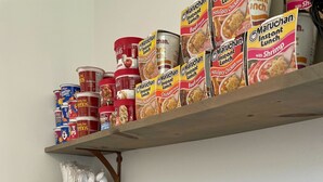 Un plan de travail de cuisine avec un four à micro-ondes, un grille-pain et un cuiseur à riz. Une étagère située au-dessus contient des conserves et des plats préparés.