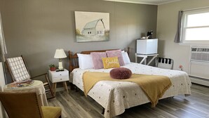 Une chambre à coucher avec un lit, une table de chevet, une lampe, une chaise et un tableau au mur.