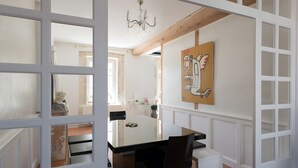 Un coin repas avec une table blanche, des chaises noires, un lustre et un tableau accroché au mur.