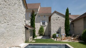 Une piscine bordée d’un muret en pierre, une pelouse et du mobilier d’extérieur.