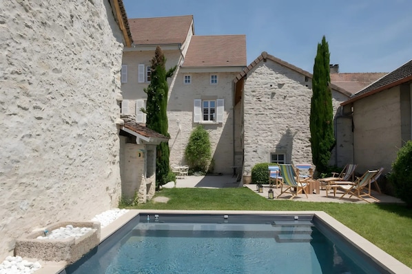 A swimming pool with a stone wall, a grassy area, and outdoor furniture.