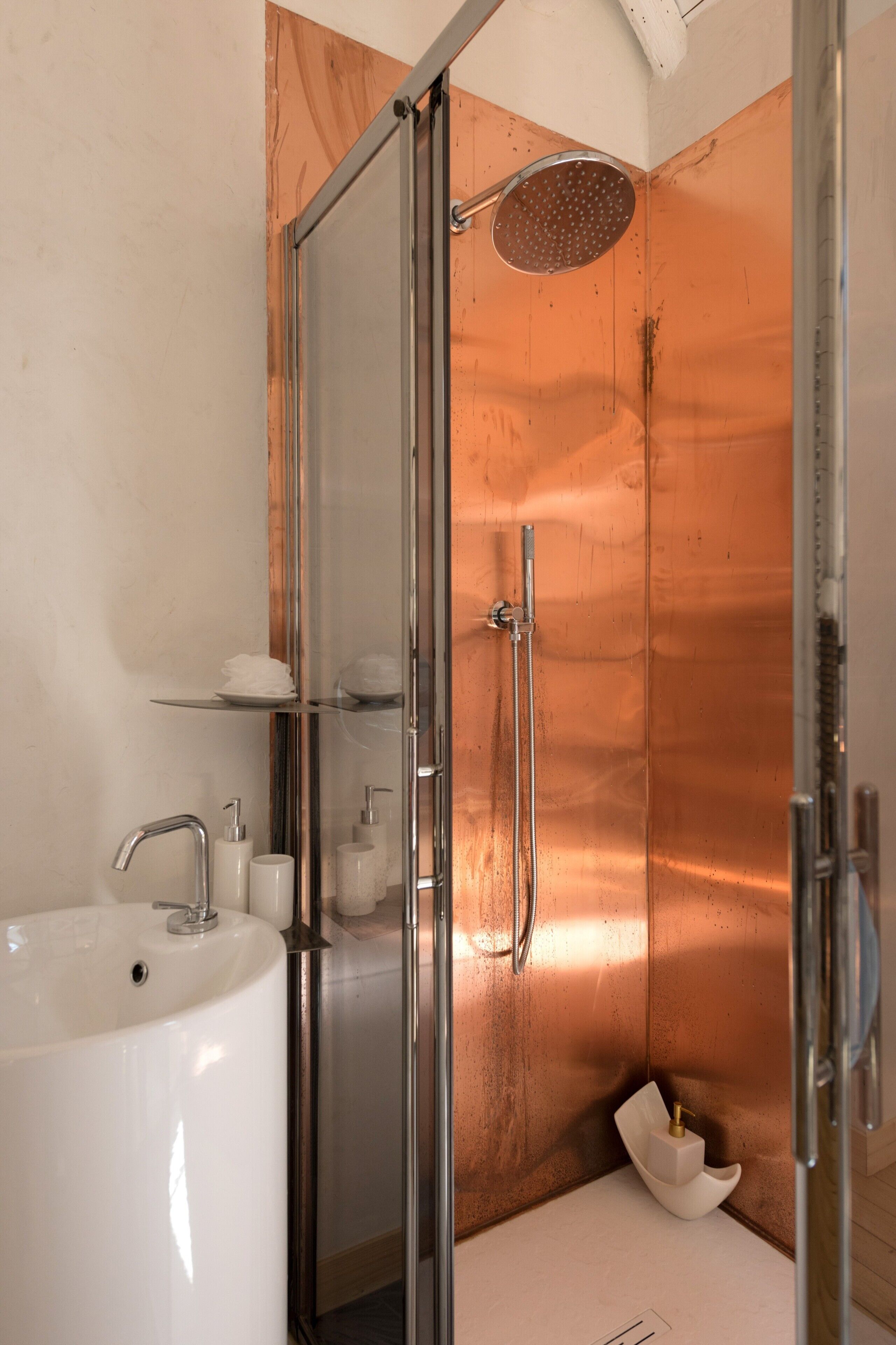 Une salle de bain moderne avec une douche à parois de verre, un lavabo blanc et un mur de couleur cuivrée.
