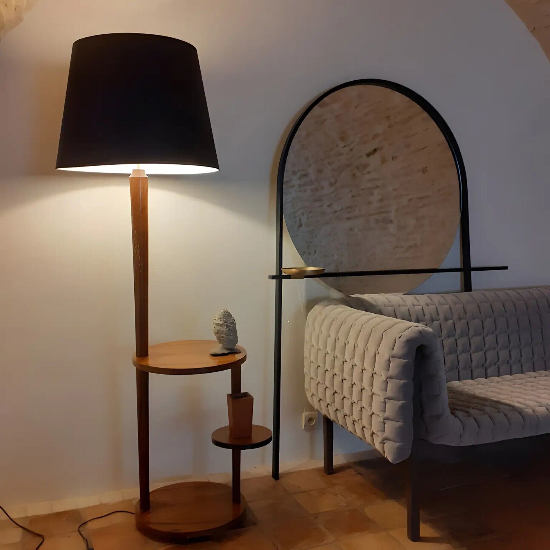 A room with a standing lamp, a round mirror, a cushioned bench, and a small table with a decorative item.