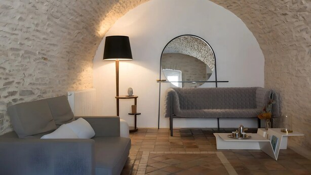 Una habitación acogedora con pared de piedra, un sofá, una lámpara, un espejo y una mesita con bandeja.