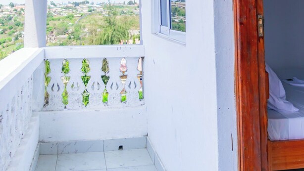 A balcony with a view of a distant landscape, a window, and a wooden door. - Yomoke Hotel Miritini (Mombasa)