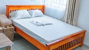 A single bed with a wooden frame, white bedding, and a small bedside table with a lamp. - Yomoke Hotel Miritini (Mombasa)