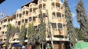 A multi-story building with balconies, surrounded by trees and market stalls. - Yomoke Hotel Miritini (Mombasa)