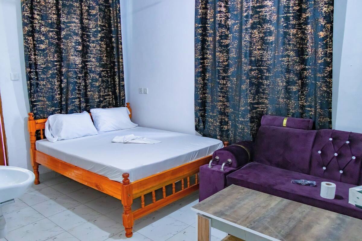 A bedroom with a wooden bed, a purple sofa, and curtains with a floral pattern.