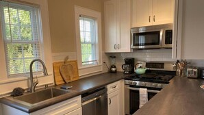 A kitchen with white cabinets, a stainless steel sink, a dishwasher, a stove, a microwave, and a coffee maker. - 3-bedroom house in charming Ocean City with AC for relaxing stays (Ocean City)