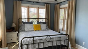 A bedroom with a metal bed frame, a bedside table, a lamp, and a window with curtains. - 3-bedroom house in charming Ocean City with AC for relaxing stays (Ocean City)