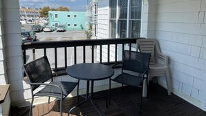 A covered outdoor seating area with a table and chairs, overlooking a street with parked cars and a building. - 3-bedroom house in charming Ocean City with AC for relaxing stays (Ocean City)