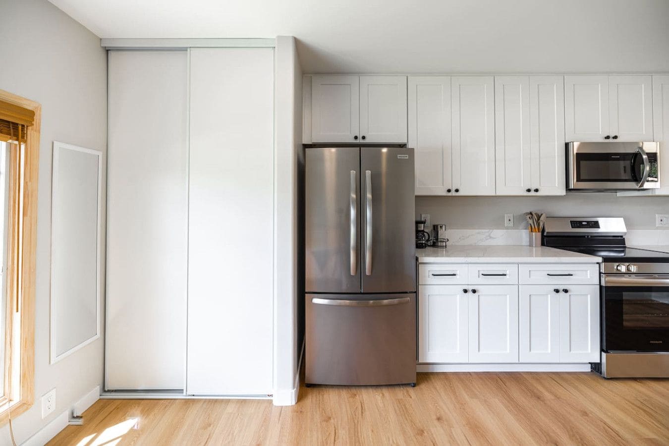 A modern kitchen with white cabinets, stainless steel appliances, and a wooden floor.