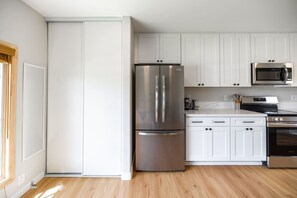 A modern kitchen with white cabinets, stainless steel appliances, and a wooden floor. - Cozy Casa | Bright Modern Suite | Kitchen + W/D (El Cajon)