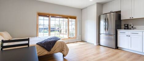 A compact kitchen with white cabinets, a stainless steel refrigerator, and a window overlooking a residential area.