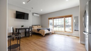 Een moderne slaapkamer met een bed, een bureau, een stoel, een televisie en een groot raam.