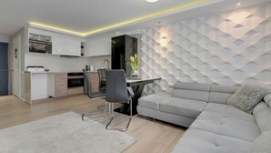 A modern kitchen with built-in appliances, a dining area with a table and chairs, and a grey sofa with a fluffy pillow. - Szafarnia 2 by Grand Apartments (Gdańsk)