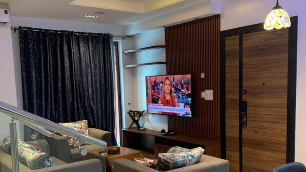 Een moderne woonkamer met een televisie, grijze banken, een eettafel en een trap.