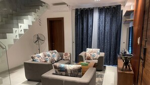 Een moderne woonkamer met een trap, grijze banken met gestreepte kussens, een houten salontafel en een ventilator.
