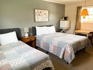 A hotel room with two beds, a small table, a TV, and a window with curtains.