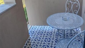 A small outdoor area with a round table and metal chairs, a patterned floor, and a view of a building in the background. - Mare Suite (Palermo)