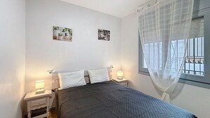 A bedroom with a bed, two bedside tables with lamps, a window with a curtain, and two wall-mounted pictures. - JARDINS I BX 27 Roses / Roses - INTERimmo (Rosas / Roses)