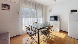A compact kitchen with a dining table, chairs, a TV, and a refrigerator. - JARDINS I BX 27 Roses / Roses - INTERimmo (Rosas / Roses)