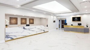 Una moderna zona de recepción de hotel con mostradores de mármol, un tragaluz y un cartel que dice "WENTILATE PALACE".