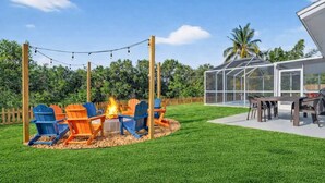 Ein Garten mit Feuerstelle, Sitzgelegenheiten und einem verglasten Patio.