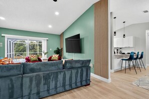 Ein modernes Wohnzimmer mit einem großen Sofa, einem Flachbildfernseher und einem Essbereich mit Barhocker.