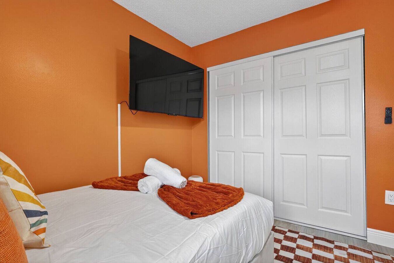 Habitación de hotel con cama, televisor montado en la pared y una puerta blanca.