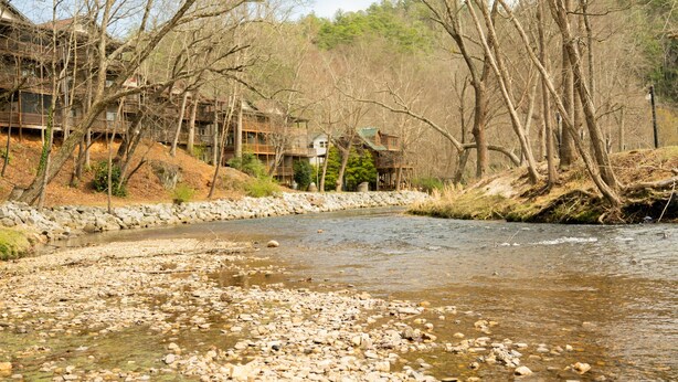 A river with rocks, trees, and a building with multiple levels and balconies.