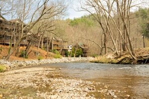 A river with rocks, trees, and a building with multiple levels and balconies. - Helen River Haus-On the River-Hot Tub (Helen)