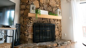 A stone fireplace with a flat-screen TV, a wooden shelf with greenery, and a black cabinet below.
