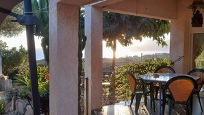 A covered patio with a table and chairs, overlooking a garden and a distant view. - House Swap Porticcio Sea View (Grosseto-Prugna)