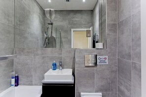 Ein modernes Badezimmer mit grauen Fliesen, einem weißen Waschbecken, einer Glasdusche und einer Toilette.