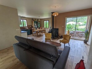 Ein geräumiger Wohnbereich mit einer Couch, einem Esstisch und Stühlen. Im Hintergrund ist eine Küche mit Herd und einer Essecke zu sehen.
