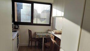 A compact kitchen with a window, wooden flooring, a small dining table, and a refrigerator. - Charming seafront apartment in Deauville (Tourgéville)