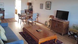 A living room with a blue sofa, wooden coffee table, and a TV on a wooden cabinet. - Charming seafront apartment in Deauville (Tourgéville)