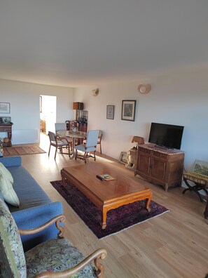 A living room with a blue sofa, wooden coffee table, and a TV on a wooden cabinet. - Charming seafront apartment in Deauville (Tourgéville)