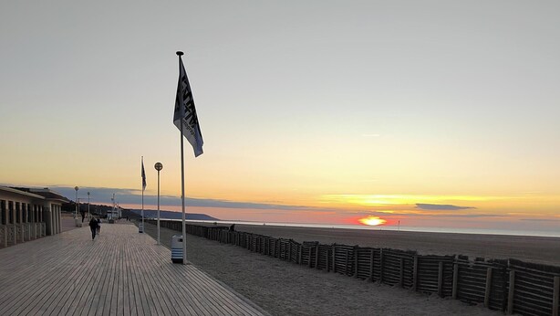 A wooden boardwalk leading to a beach with a sunset in the background. - Charming seafront apartment in Deauville (Tourgéville)